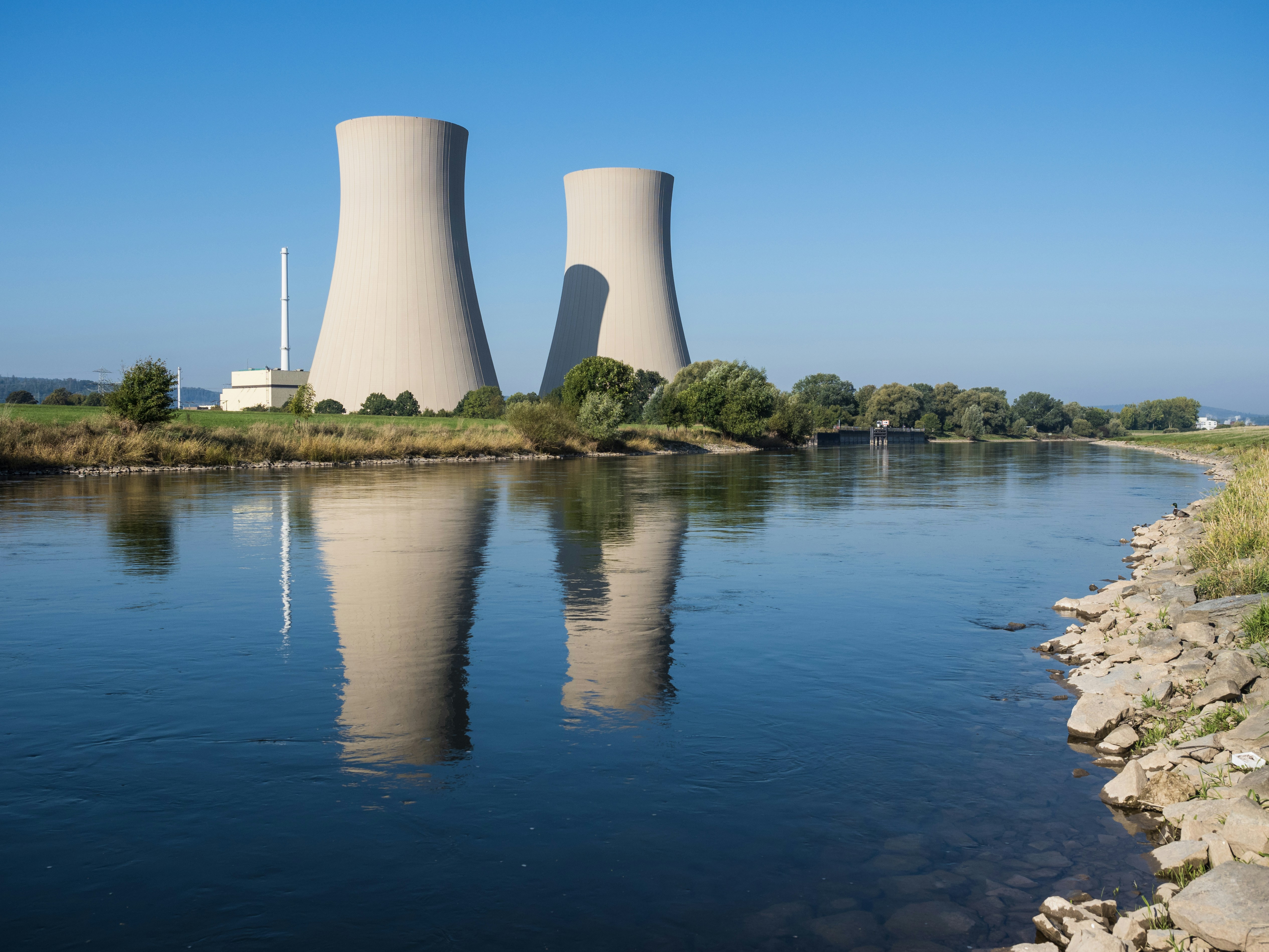 A nuclear power plant reflected in a calm river, illustrating water-related nature risk.
